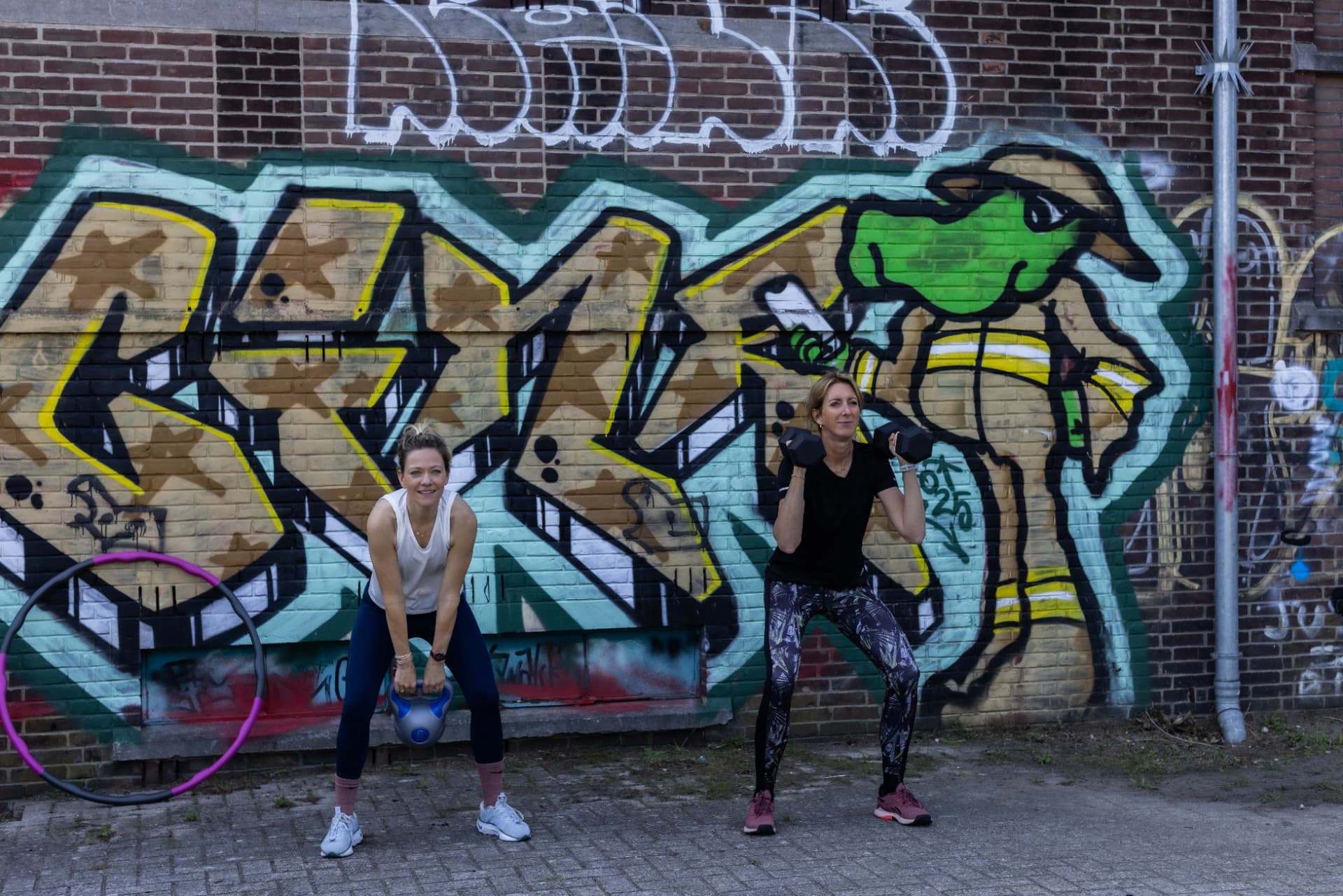 Twee vrouwen doen buiten krachttraining met een kettlebell en halters